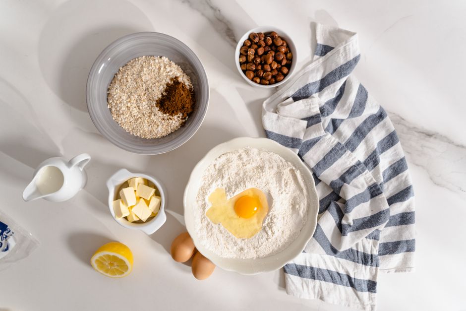 Flat lay of baking ingredients like flour, egg, and nuts ready for preparation on a marble counter.