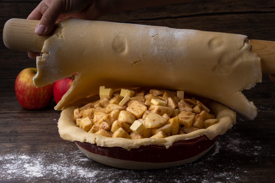Rolling out dough for homemade apple pie with fresh apple chunks and buttery crust.